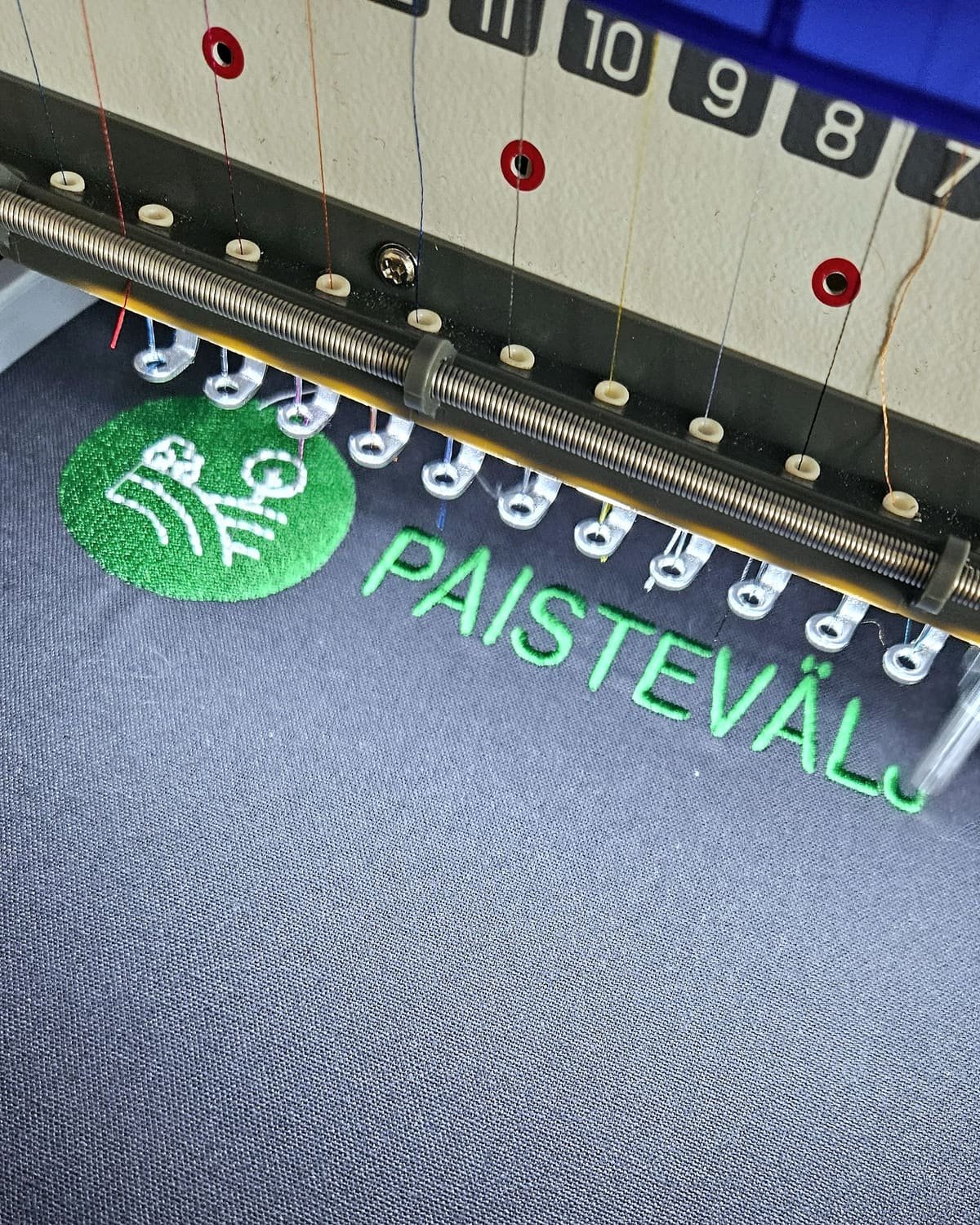 Embroidery machine needles stitching a green logo onto dark fabric