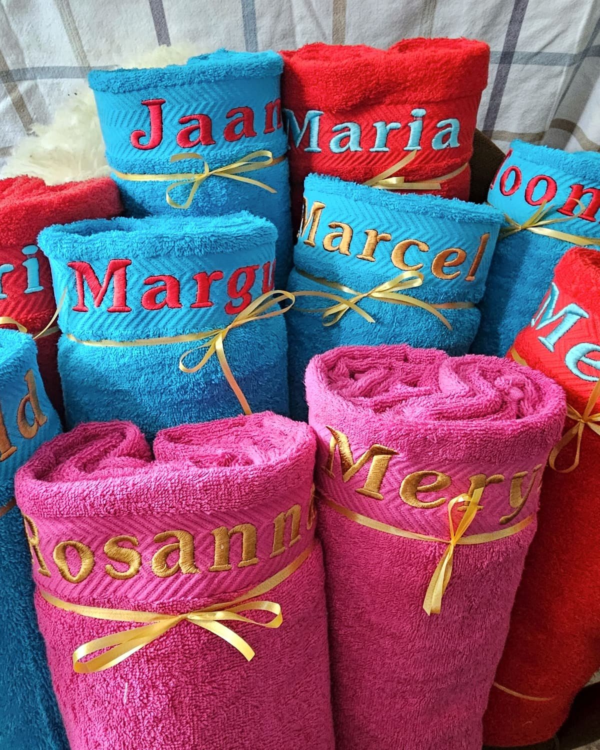 Ten rolled sauna towels, each with an embroidered name and a gold ribbon