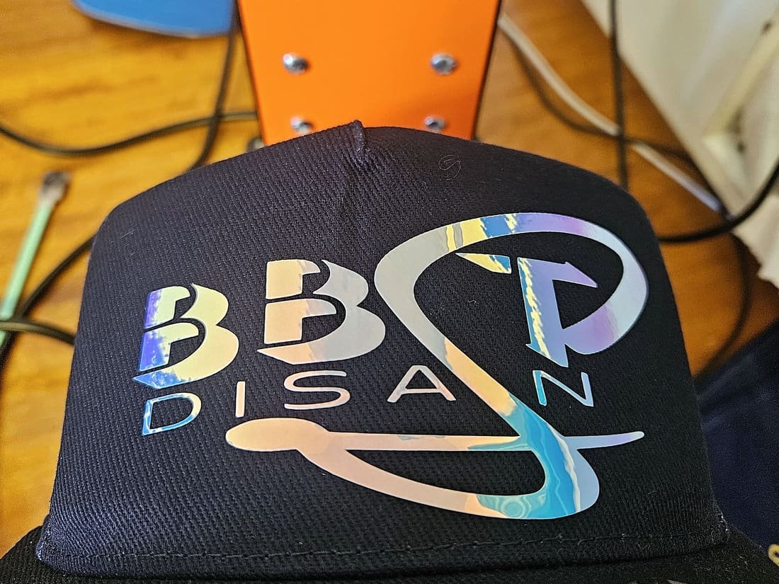 Black cap with a holographic BBST Disain logo in front of the cap press