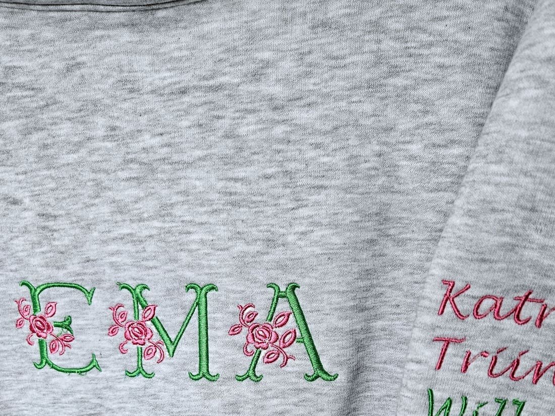 Grey sweatshirt with an embroidered floral monogram and names on the sleeve